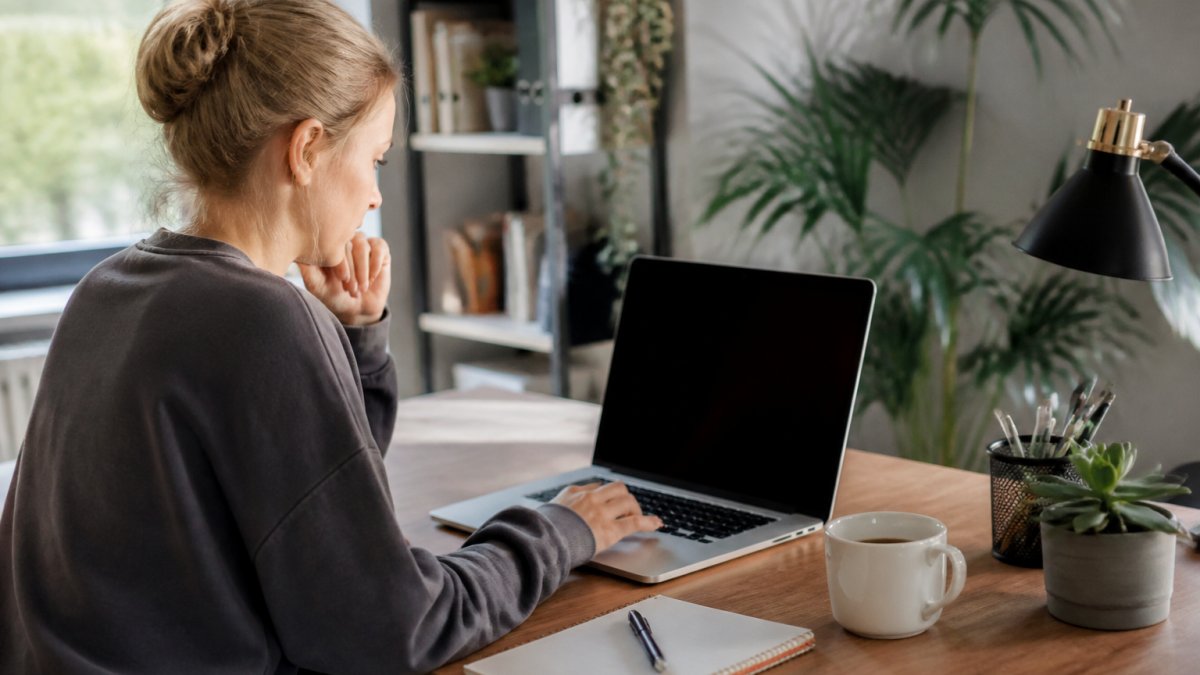 A person working on a laptop at a tidy home desk, with a notebook and coffee nearby, looking focused while building a website